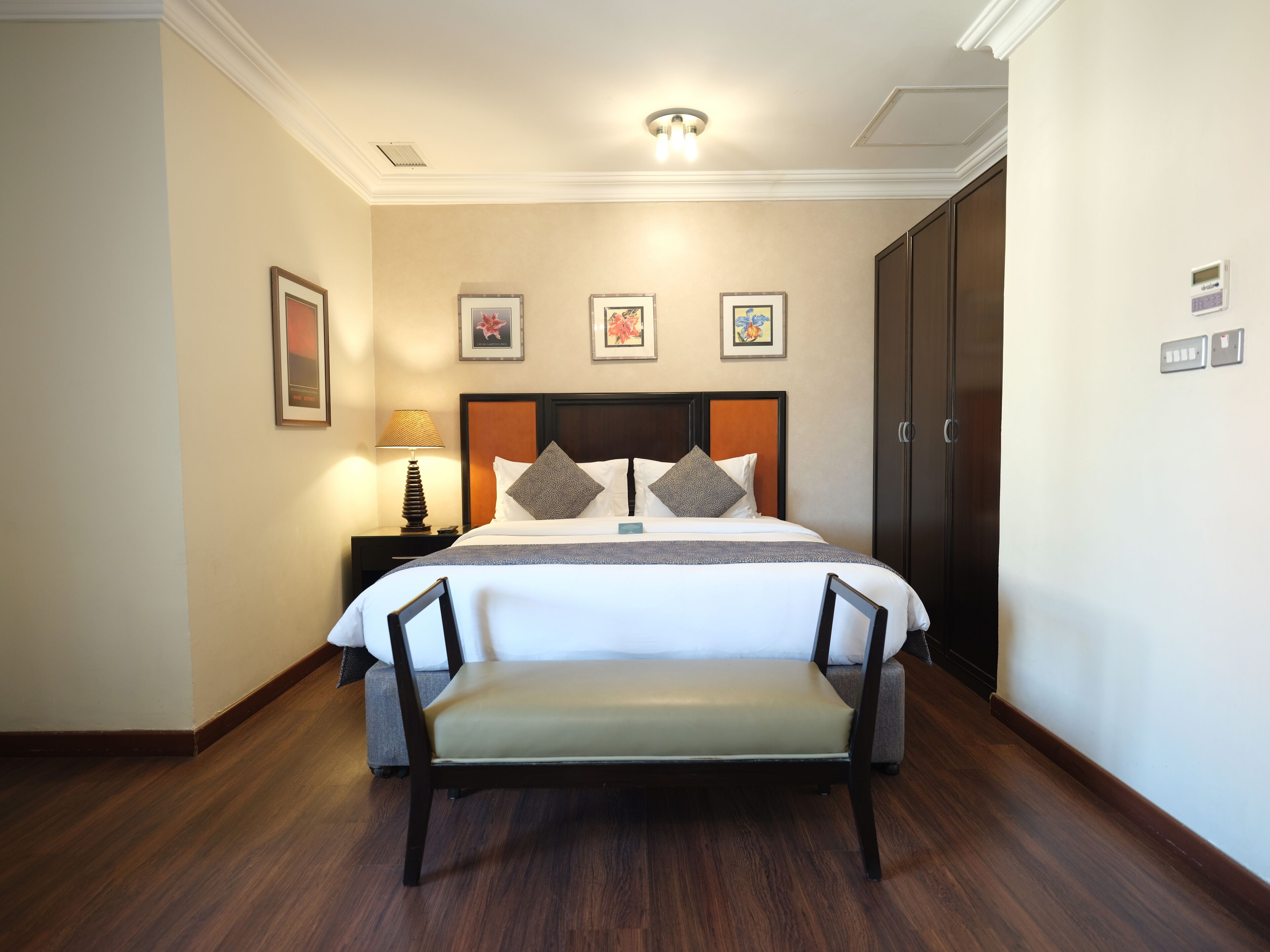 Habitación de hotel con una cama grande, una mesita de noche con lámpara, un banco y un armario.
