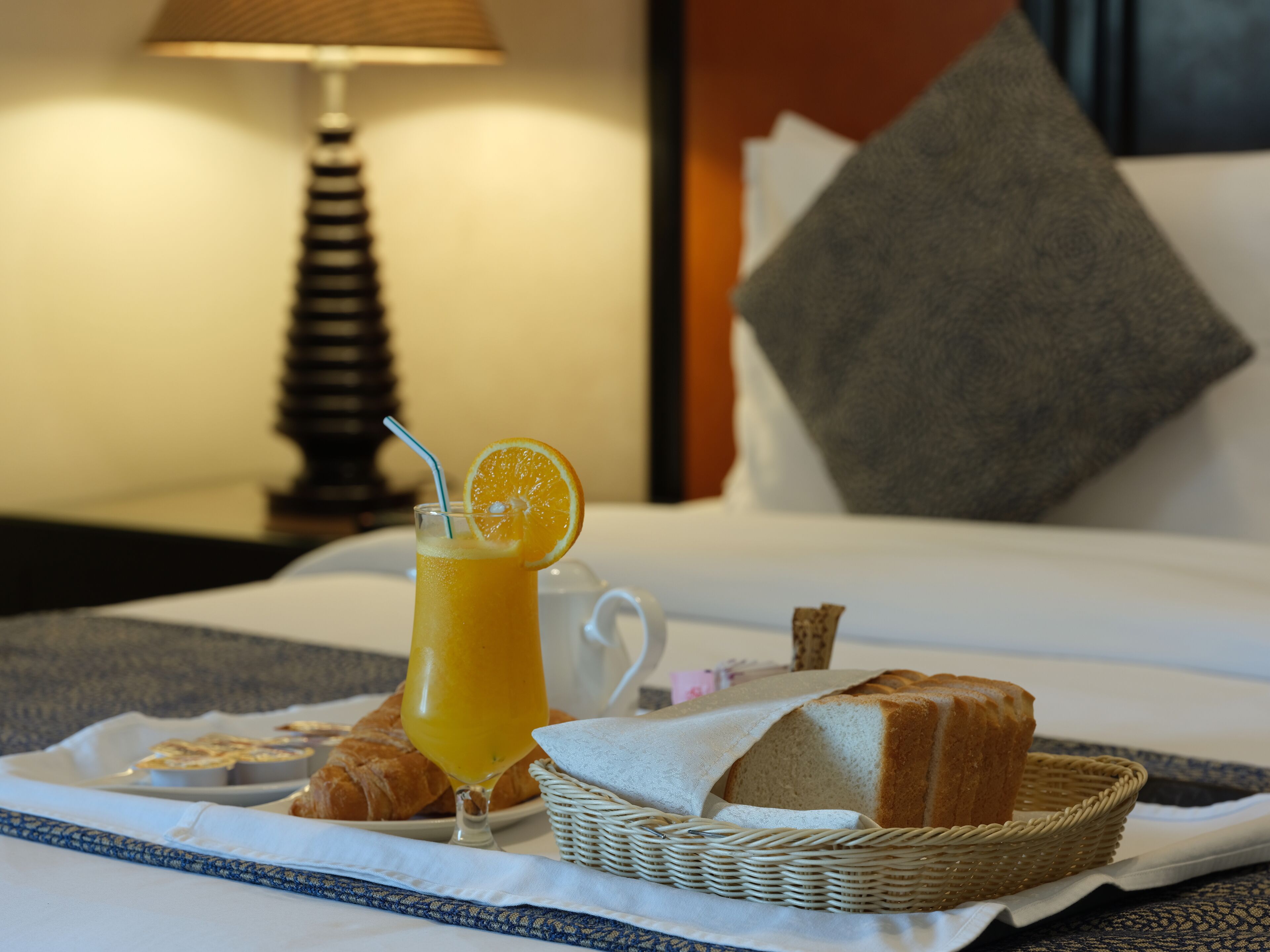 A breakfast setup with a glass of orange juice, a croissant, and a loaf of bread on a tray.