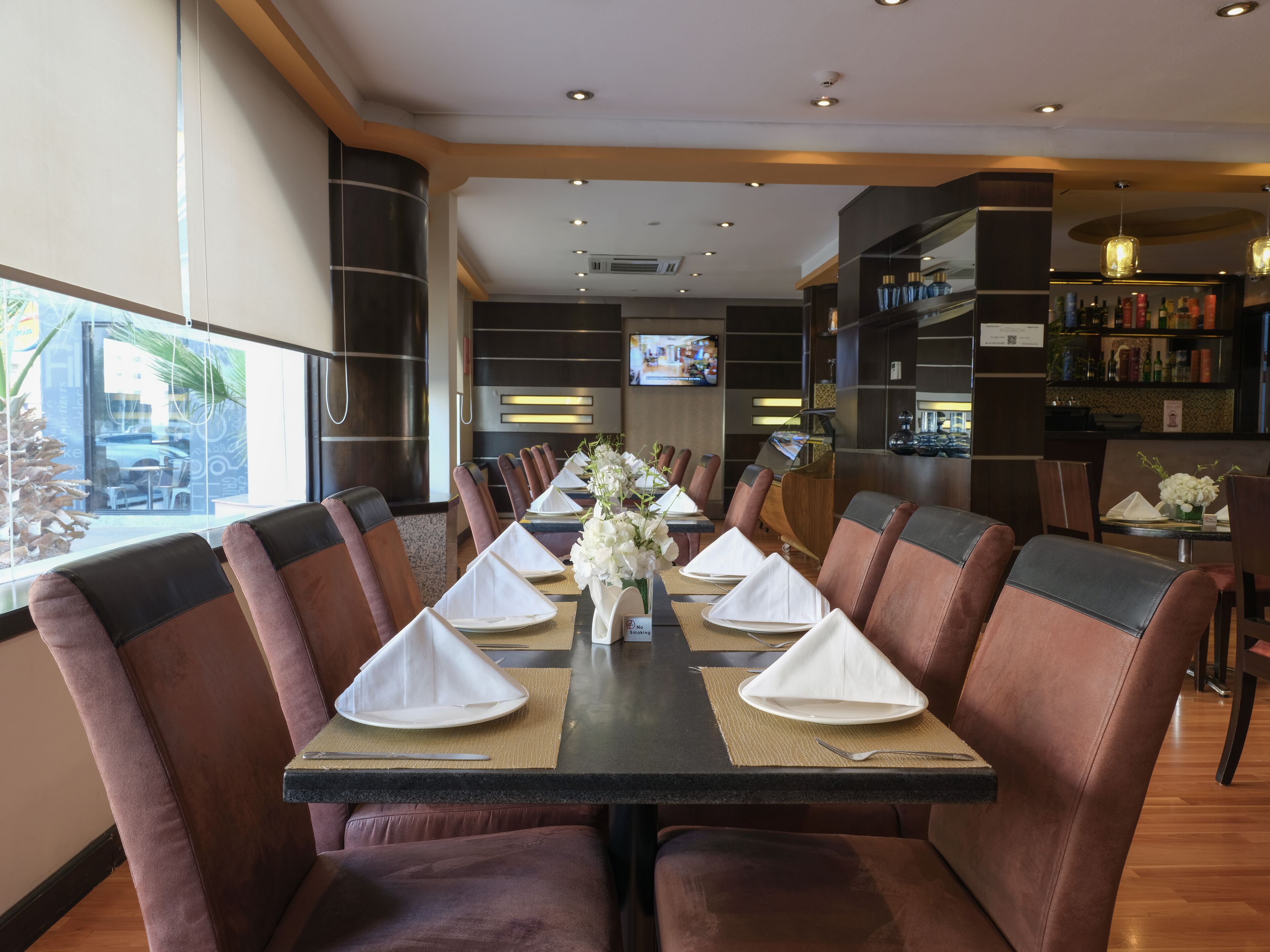 A restaurant with a long table set for a meal, surrounded by leather chairs, with a view of the outside.
