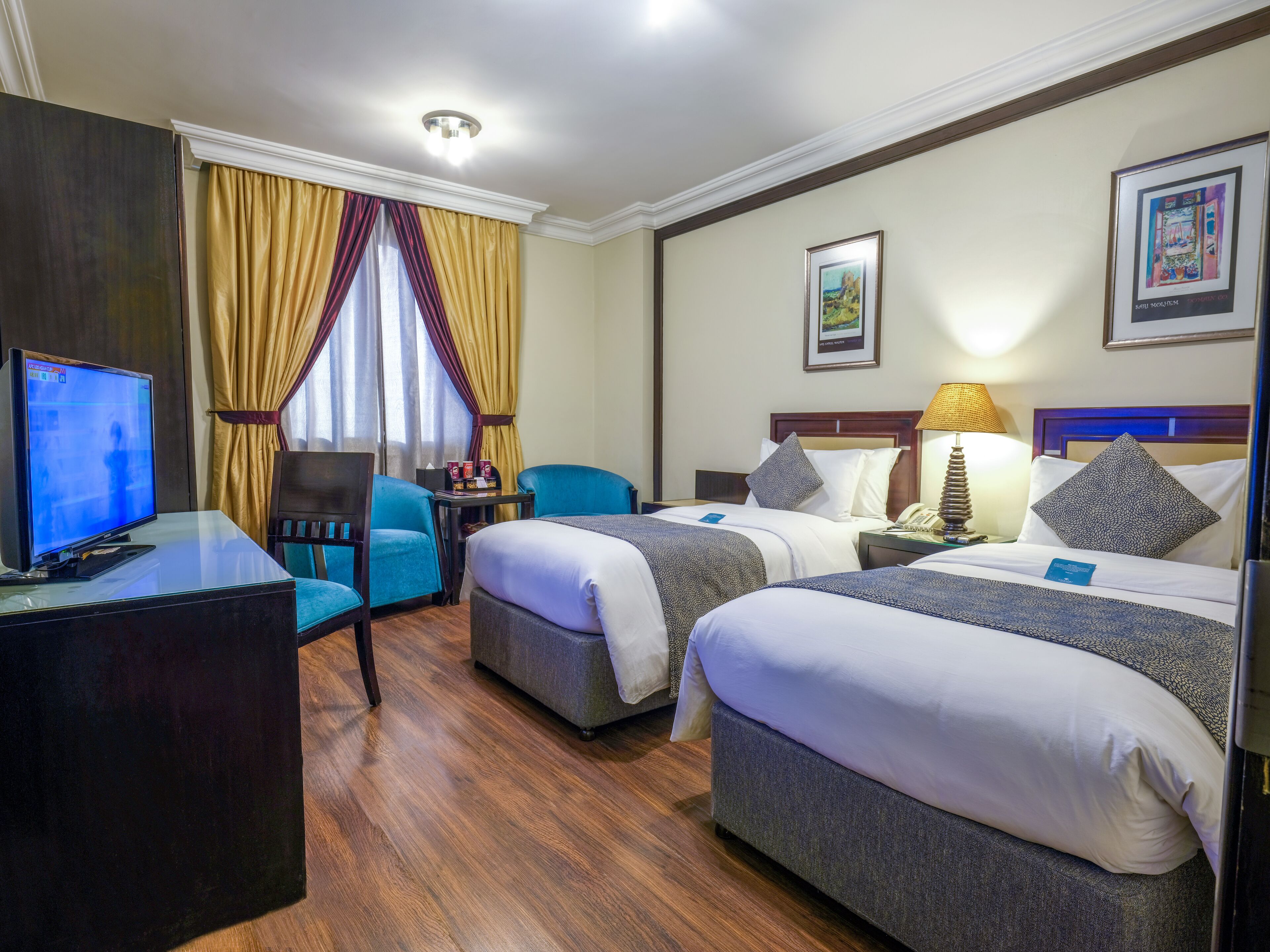 Une chambre d’hôtel avec deux lits, un bureau avec un ordinateur, une chaise et une lampe.