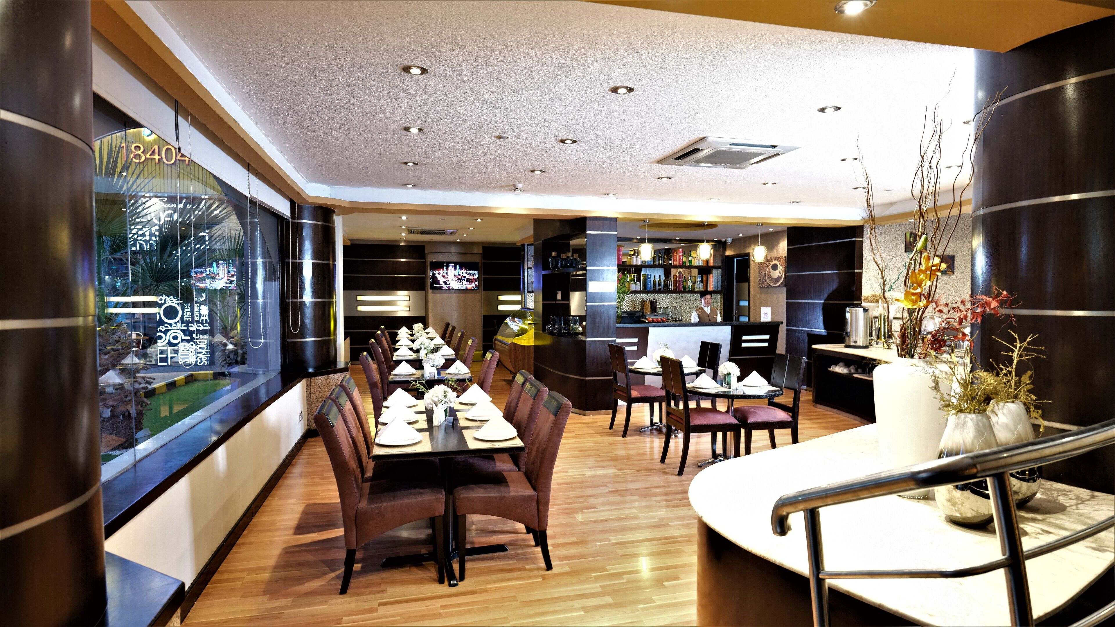 Um restaurante com soalho de madeira, área de bar e disposição de mesas e cadeiras.