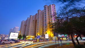 A multi-story hotel with illuminated signage, a parking lot, and surrounding urban buildings. - Boudl Kuwait (Salmiya)