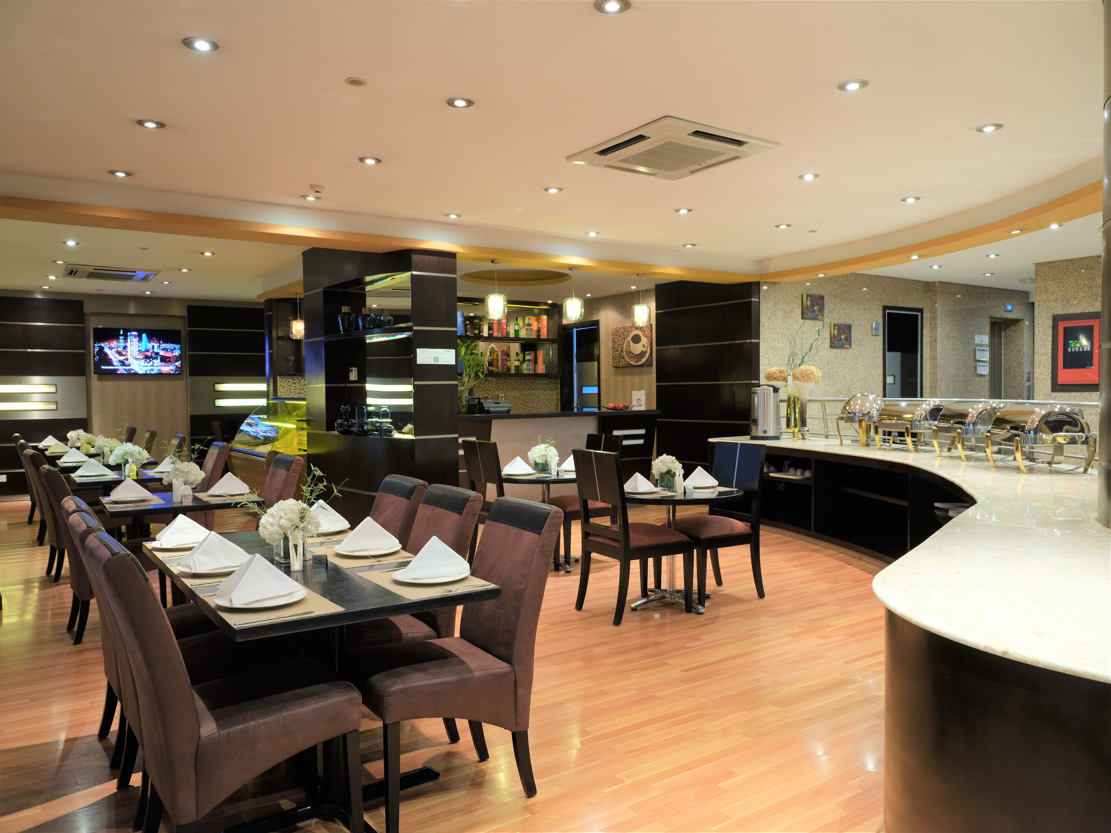 A restaurant with multiple dining tables set for guests, a bar area, and a television displaying a cityscape.