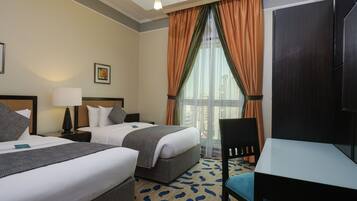 Une chambre d’hôtel avec deux lits, un bureau, une chaise, une lampe, un tableau au mur et une fenêtre avec des rideaux.