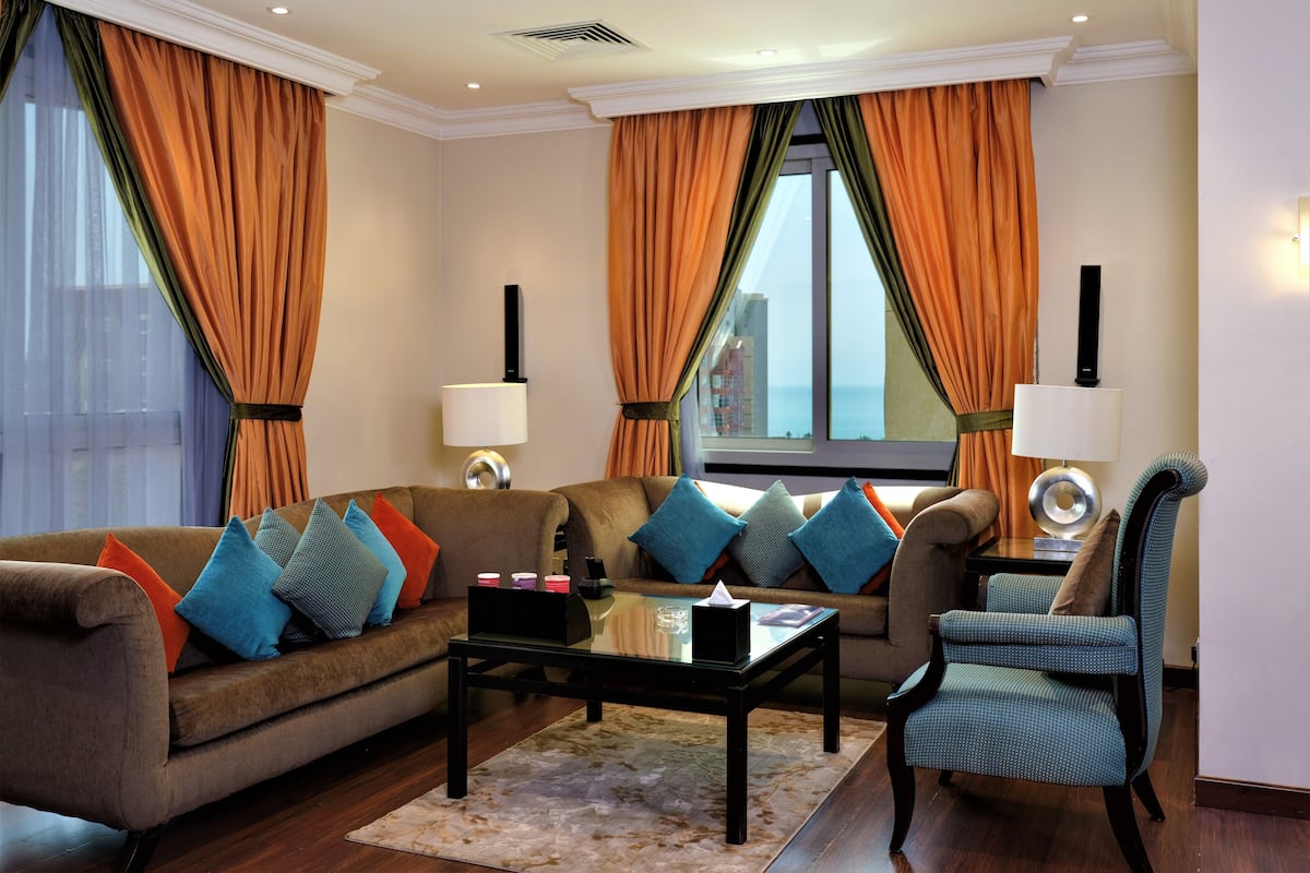 A living room with a sofa, armchairs, a coffee table, and a view of the ocean through large windows.