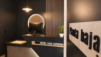 A reception desk with a computer, a potted plant, and a sign reading 'HOTEL CASA GARDENIA.'
