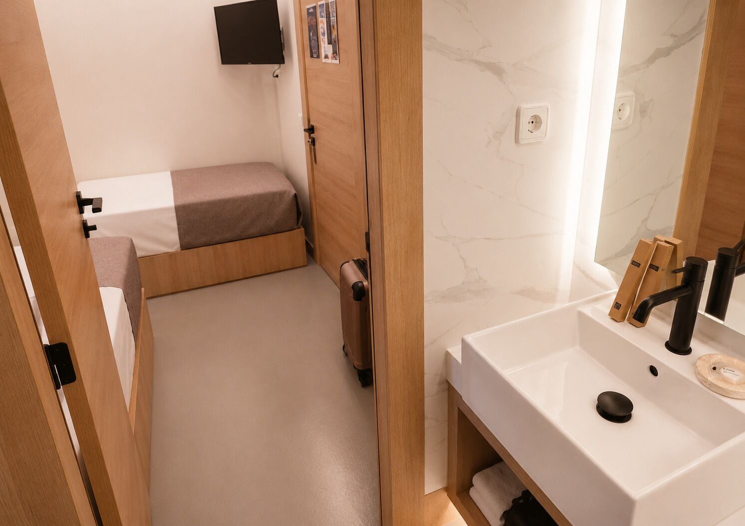 A compact room with a bed, a small desk, a mirror, and a sink.