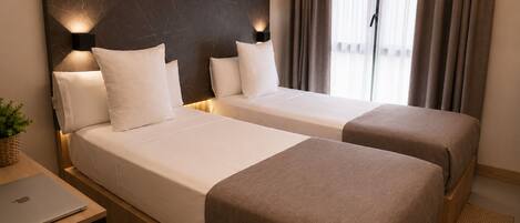 A hotel room with two beds, a desk with a laptop, and a window with curtains.