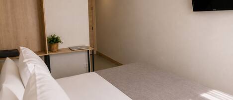 A hotel room with a bed, a desk with a laptop, a wall-mounted TV displaying 'NETFLIX', and a wooden wardrobe.