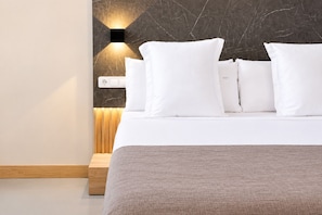 A neatly made bed with white bedding and pillows, a wooden bedside table, and a wall-mounted light fixture. - Hotel Casa Gardenia by Blossom Hotels (Barcelona)