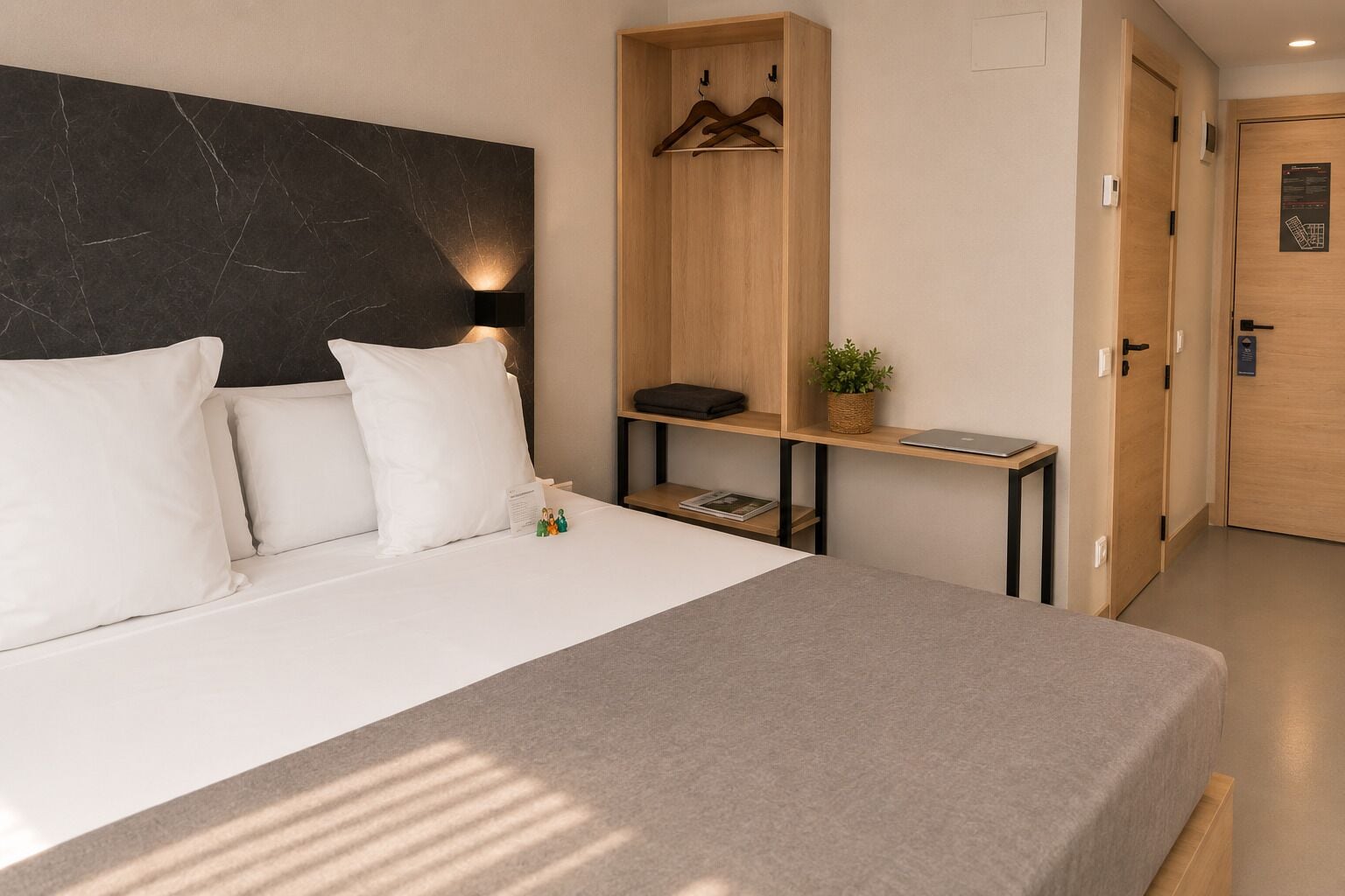 Una habitación de hotel moderna con una cama grande, un armario de madera, un escritorio pequeño y una lámpara fijada a la pared.