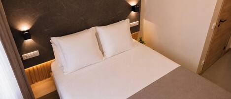 A hotel room with a bed, a headboard, bedside lamps, and a door.