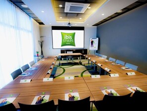 Uma sala de conferências com uma tela grande exibindo 'ibis Styles Hotels', uma mesa comprida com cartões de nome e um projetor.