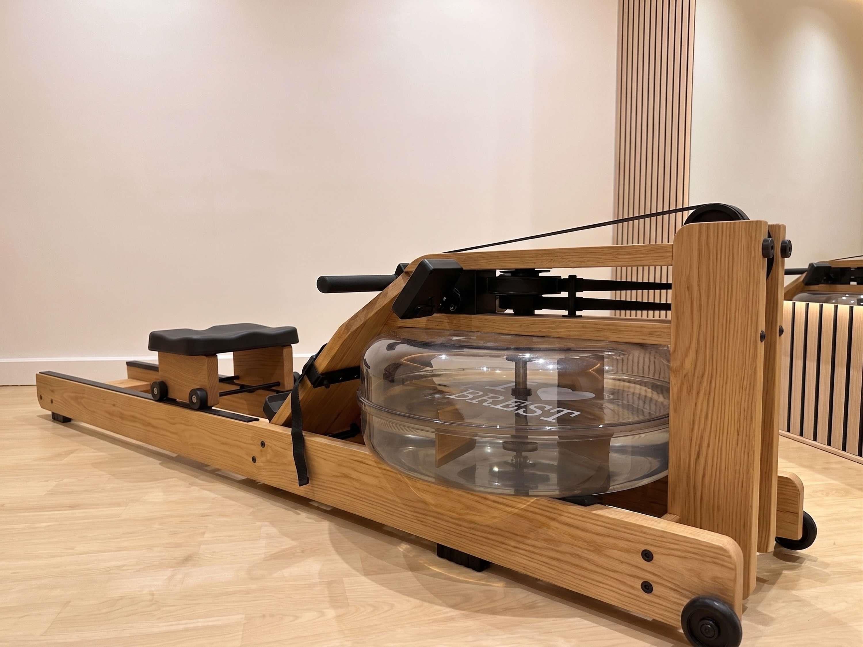 Uma máquina de remo de madeira com volante transparente, pegas pretas e rodas.