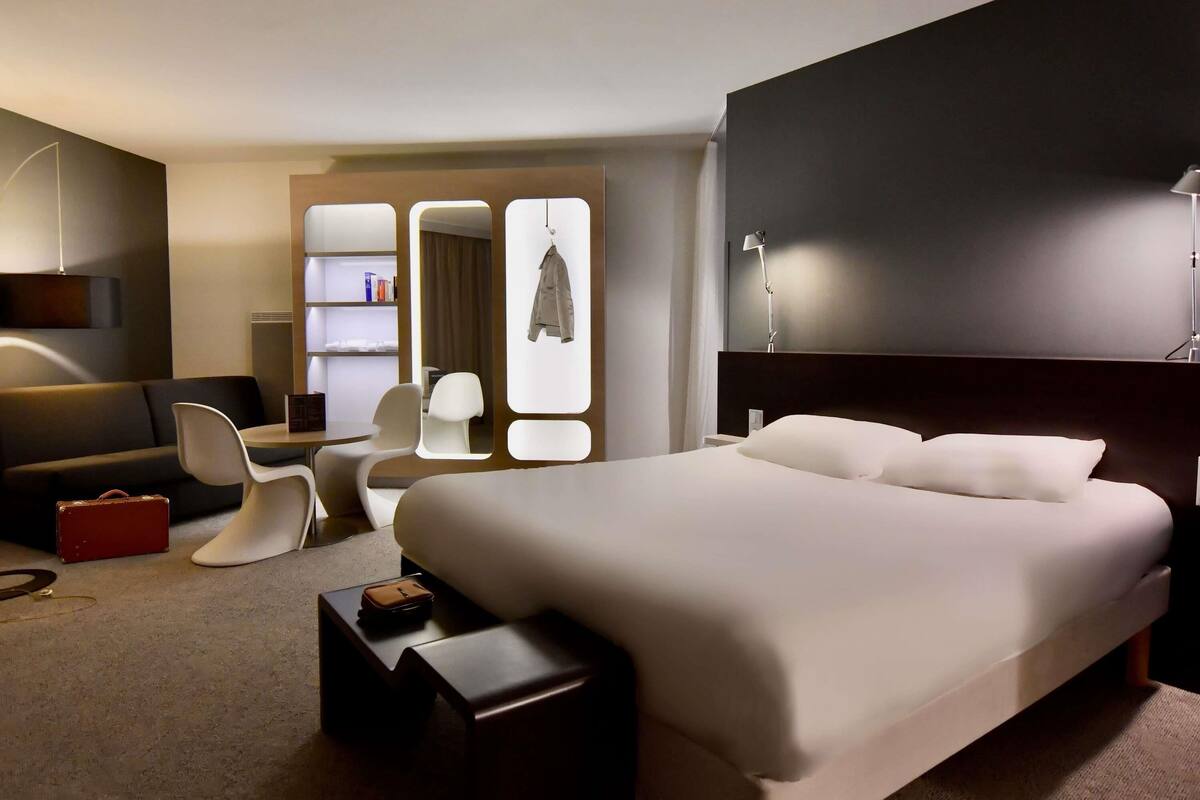 Una habitación de hotel moderna con una cama grande, un escritorio, una silla, un armario y un espejo.