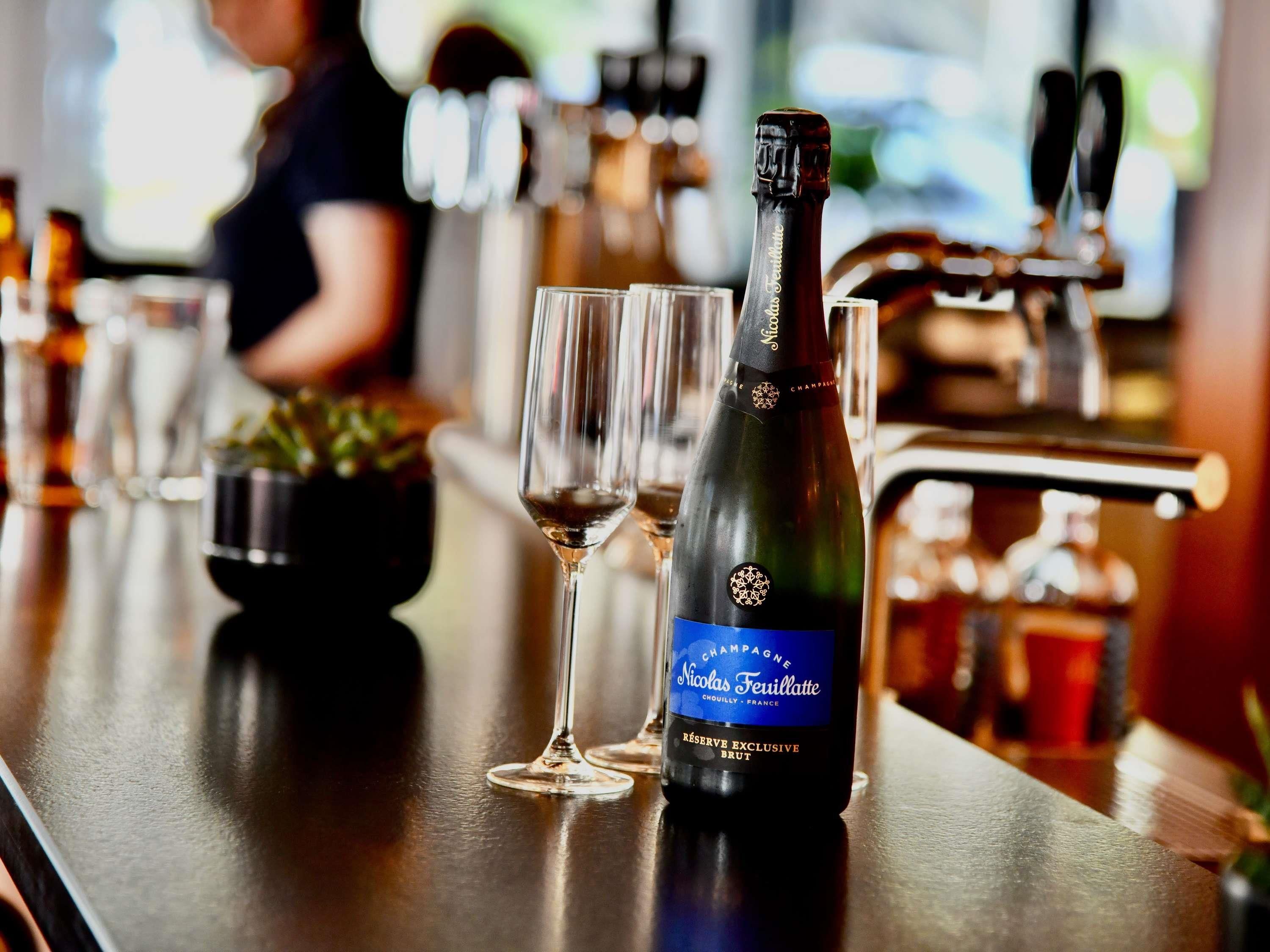 A bottle of Nicolas Feuillatte champagne on a bar counter with two glasses.