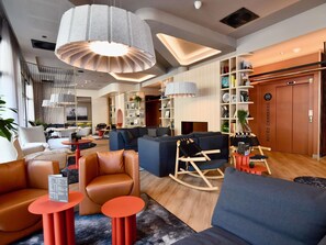 Un moderno vestíbulo de hotel con zonas de estar, un mostrador de recepción y una estantería.