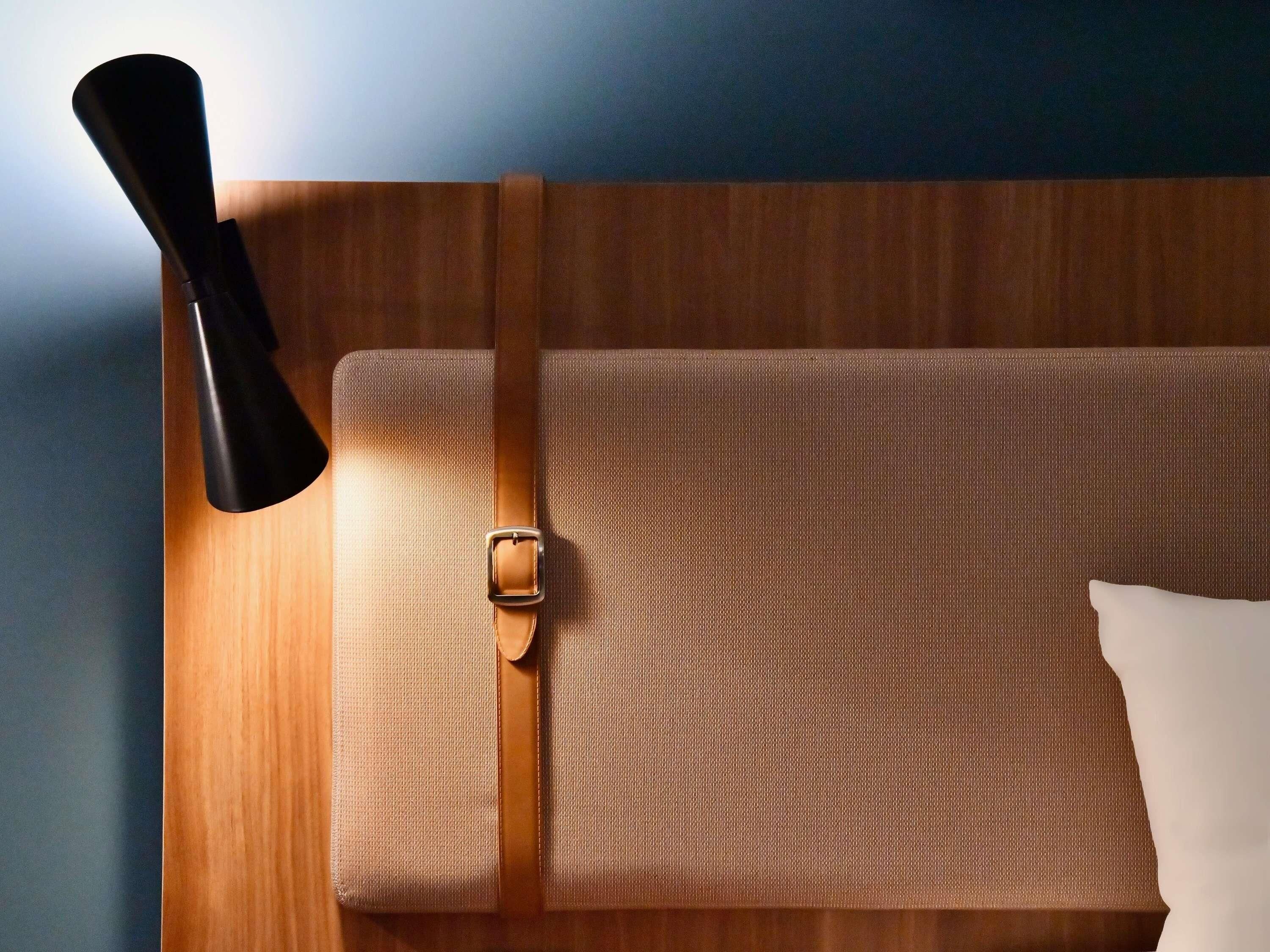 A neatly made bed with a white pillow, a wooden headboard, and a black object on the left.