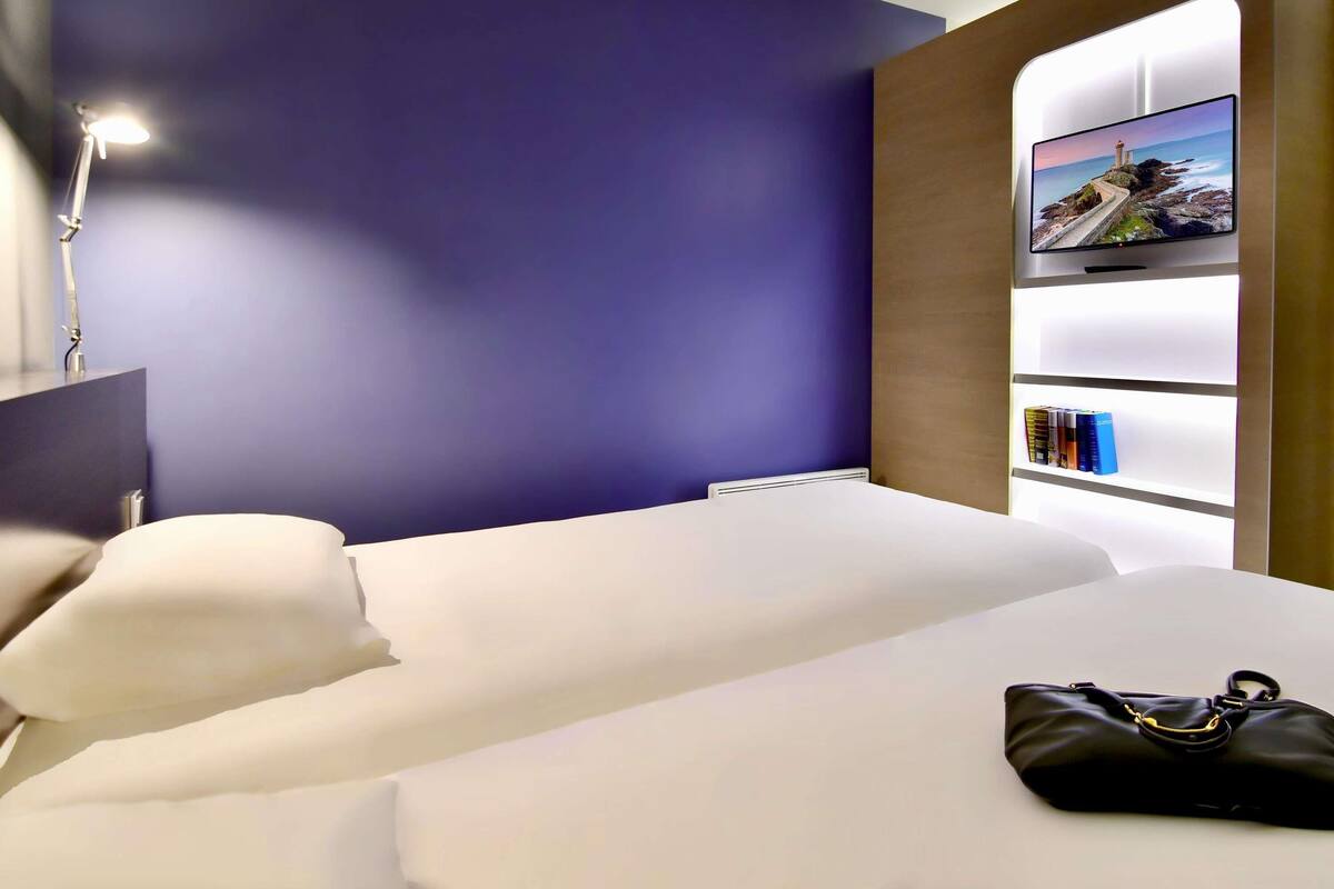 Una habitación de hotel moderna con una cama, una mesita de noche, una lámpara, un televisor y una estantería.