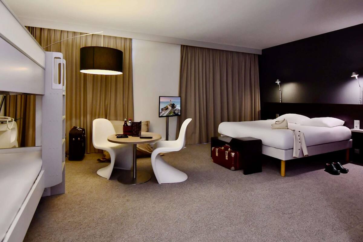 Una habitación de hotel con cama, escritorio, silla, lámpara y vista al mar.
