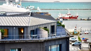 Un edificio moderno con techo plano, ventanas amplias y un balcón con vistas a un puerto deportivo con barcos.