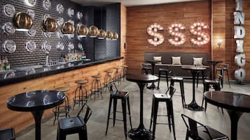 A bar area with a brick wall, round tables, and stools.