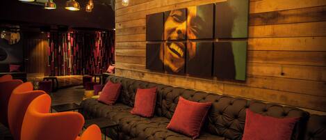 A modern lounge area with a tufted sofa, vibrant orange chairs, and a large wall art piece.