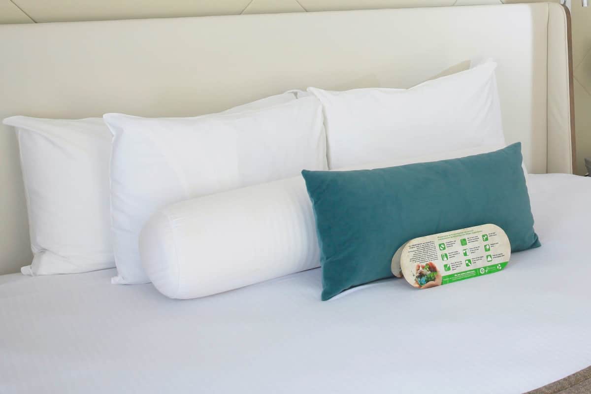 A bed with white pillows and a teal pillow with a recycling symbol.