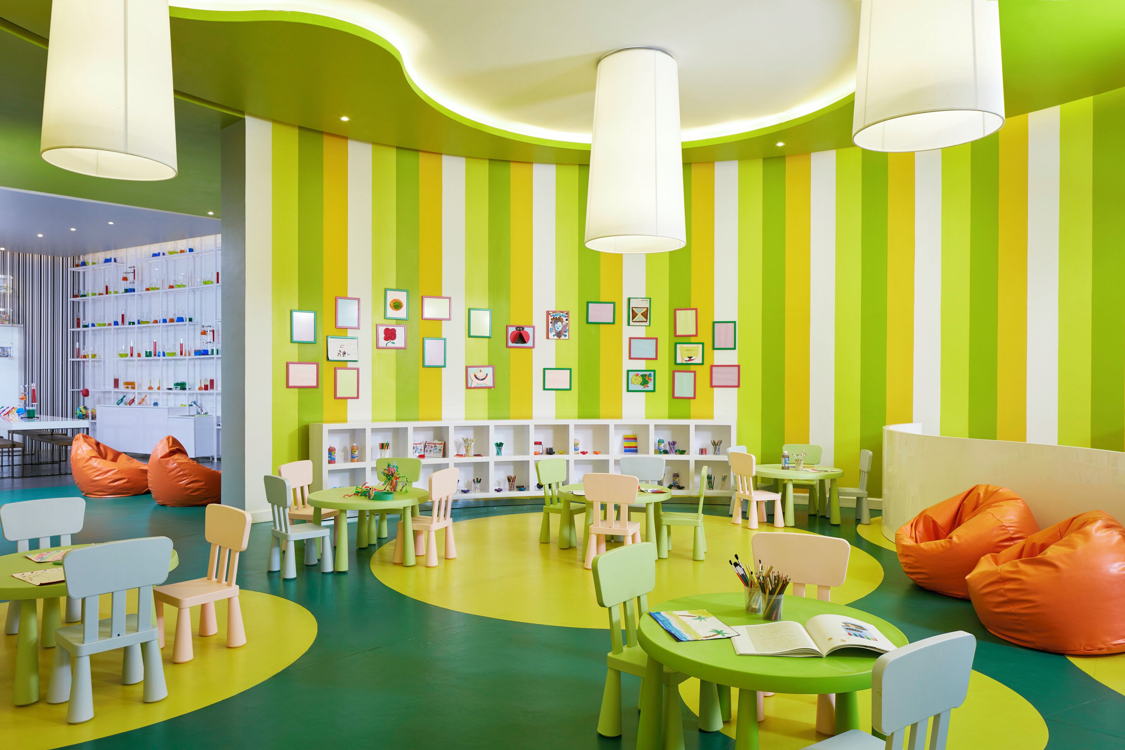 A brightly colored children's playroom with striped walls, multiple tables, chairs, and bean bags.