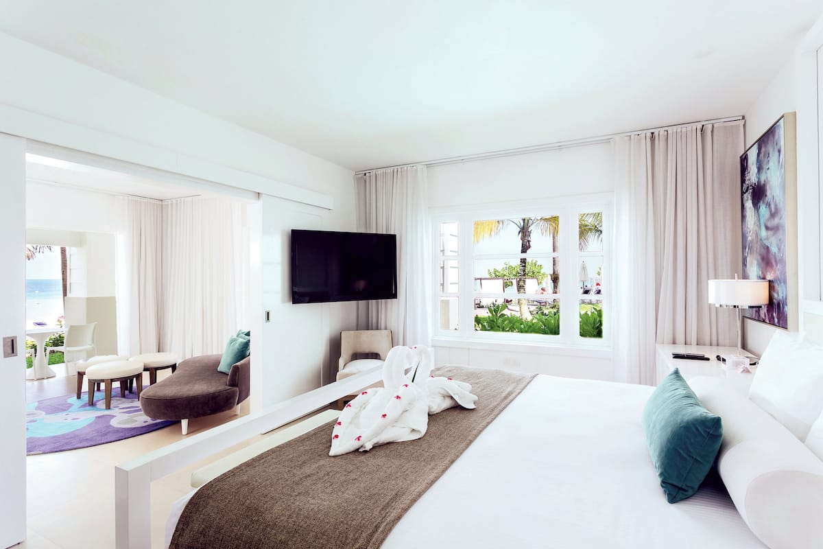 A hotel room with a bed, a TV, a sofa, a chair, and a window with a view of greenery.