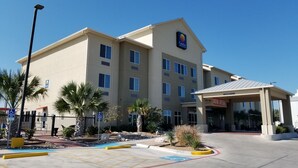 A hotel with a parking lot, palm trees, and a covered entrance.