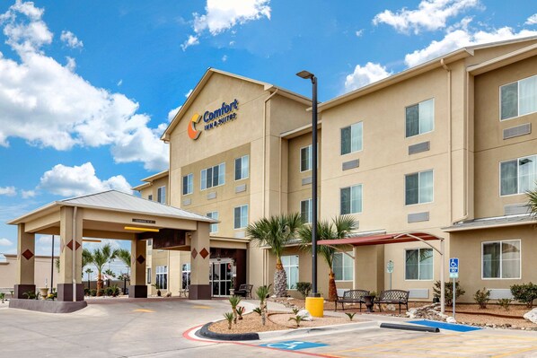A Comfort Inn & Suites hotel with a covered entrance, palm trees, and a wheelchair-accessible sign.
