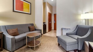 A modern hotel room with a grey sofa, a small round table, a grey armchair, and a lamp. - Comfort Inn & Suites Lakeside (Eagle Pass)