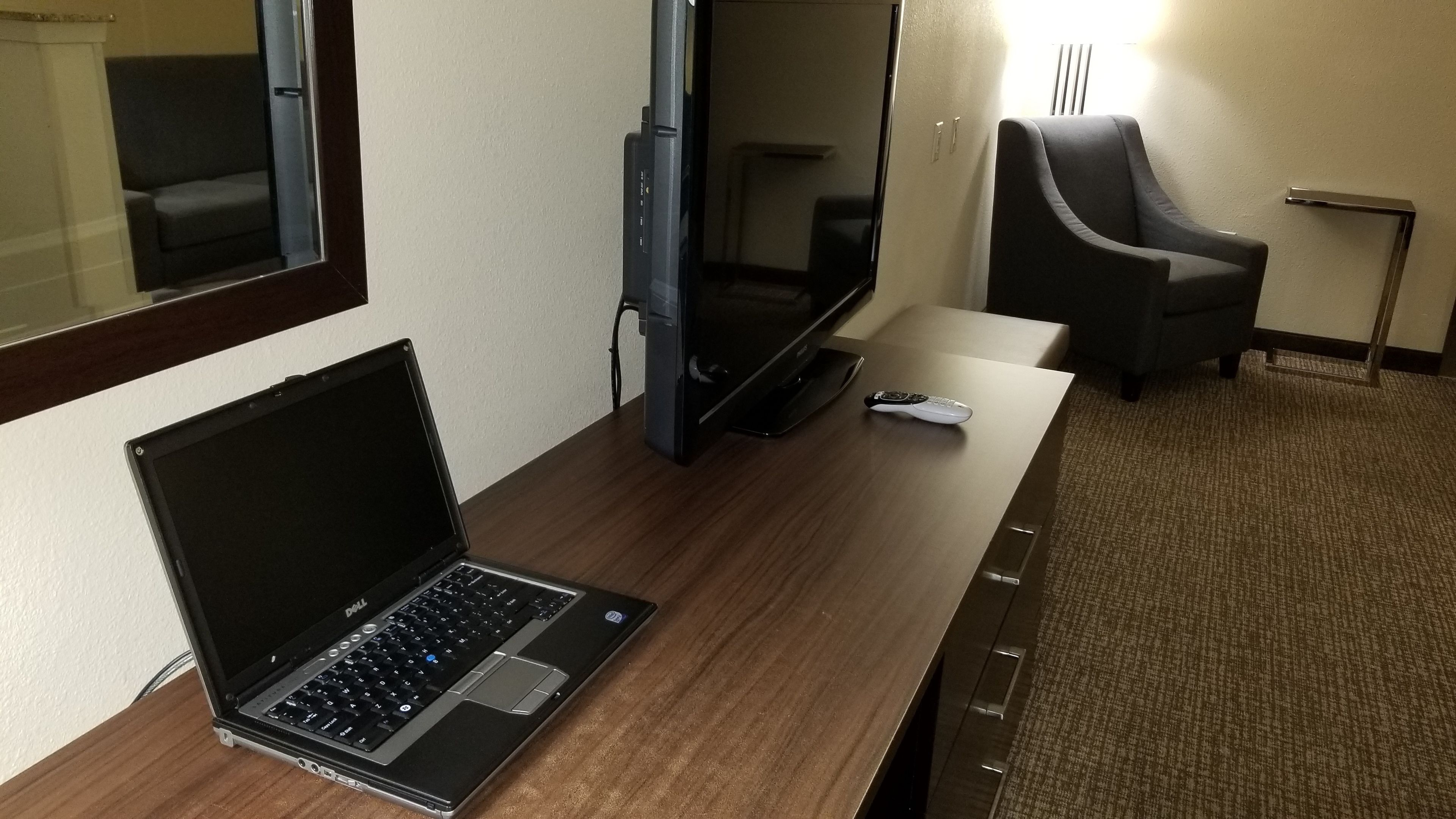Ein Hotelzimmer mit einem Holztisch, einem Laptop, einem Fernseher und einer Fernbedienung.