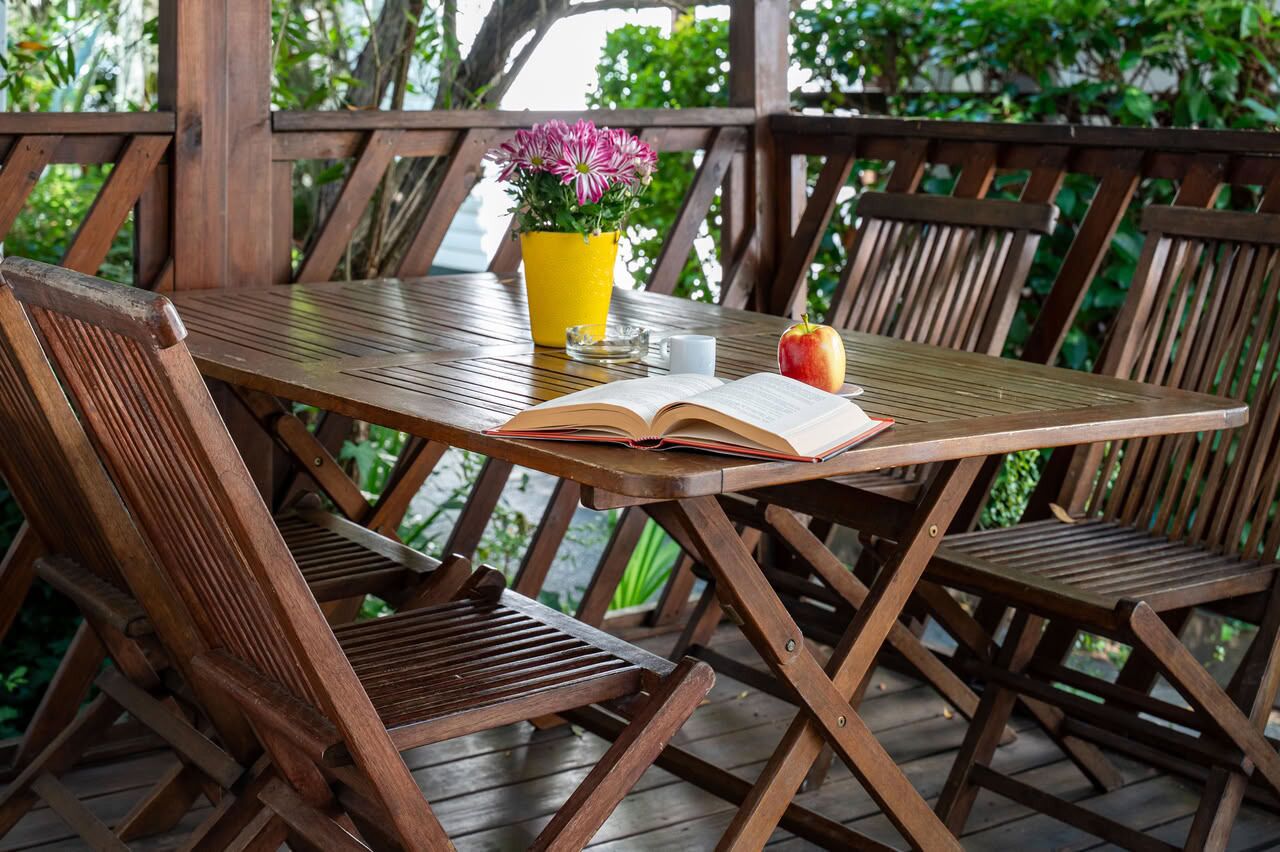 A wooden table with an open book, a yellow flower pot, and an apple.
