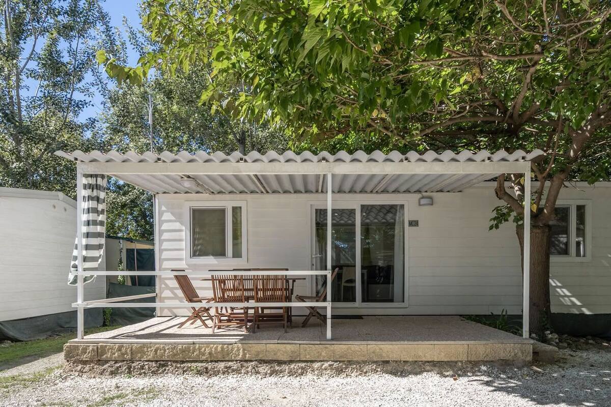 Un espacio de estar al aire libre con techo, con una mesa, sillas, una pérgola y un árbol.