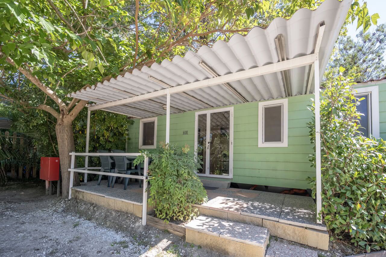 A green house with a covered porch, a small table, and chairs.