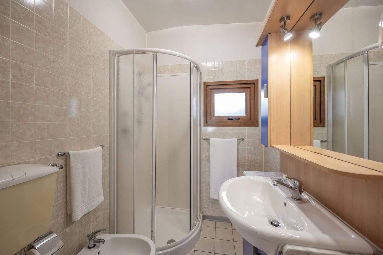 A bathroom with a glass shower enclosure, a sink, a toilet, and a window providing natural light.