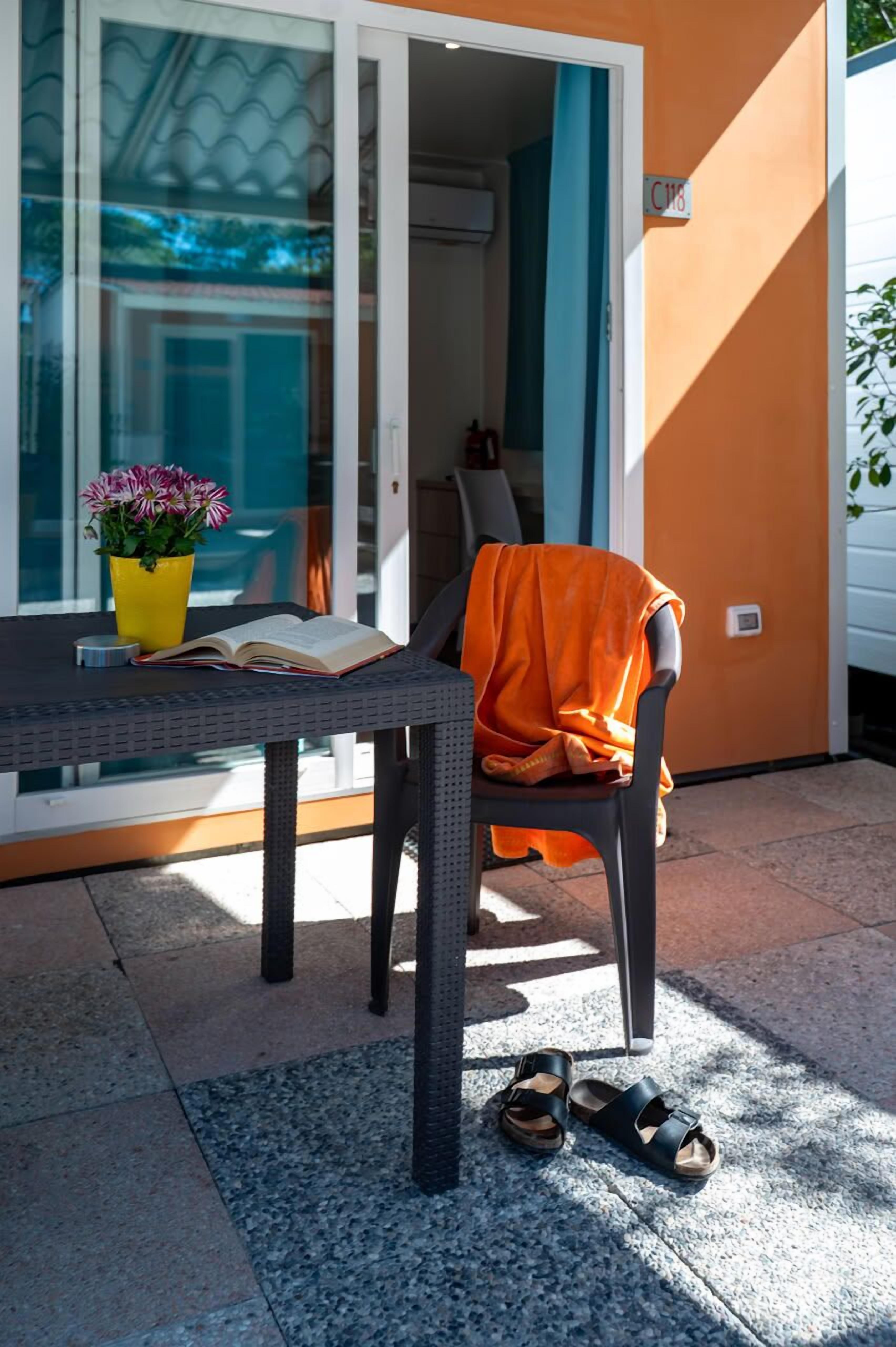 Un espacio al aire libre con una mesa, una silla, una planta en maceta y un par de sandalias en el suelo.