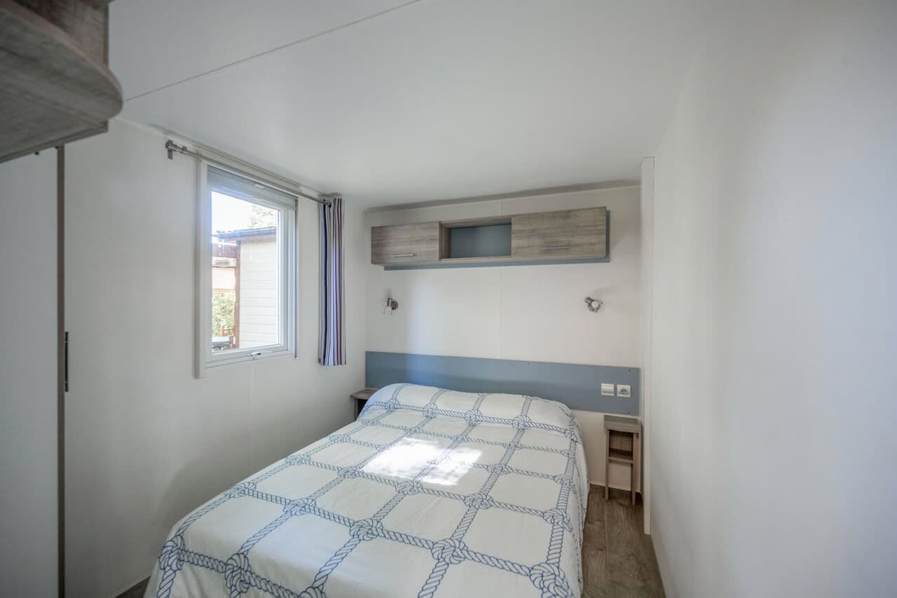 A bedroom with a bed, a window with curtains, a bedside table, and a built-in shelf.