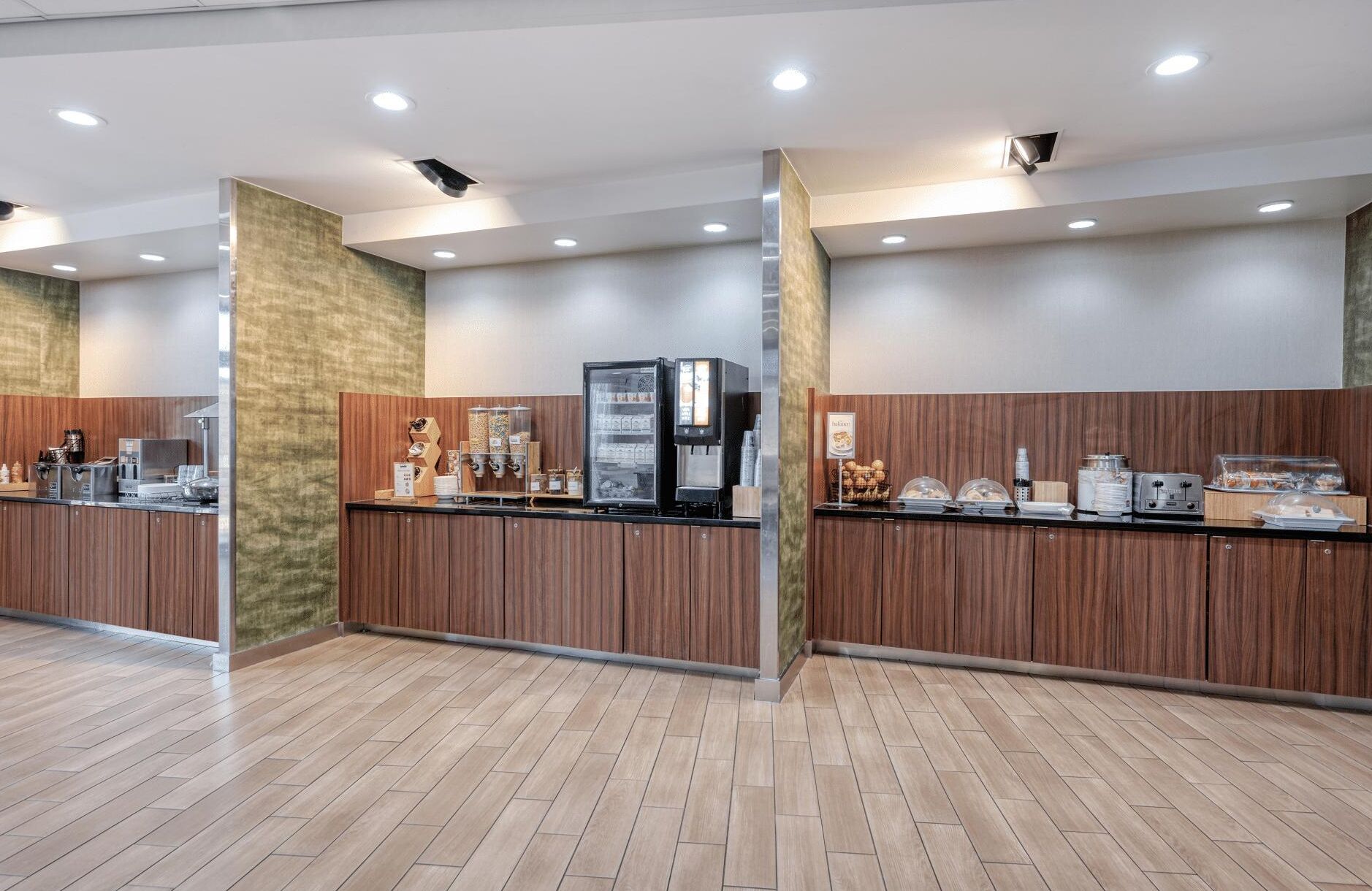 Una zona de recepción moderna con un mostrador de madera, máquinas de café y una estación de bebidas de autoservicio.
