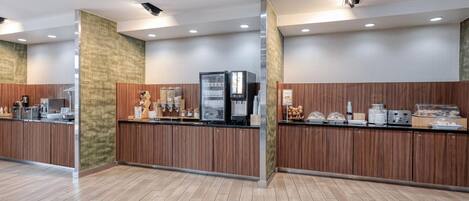 Una zona de recepción moderna con un mostrador de madera, máquinas de café y una estación de bebidas de autoservicio.