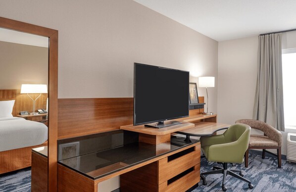 Una habitación de hotel con una cama, un escritorio con televisor, una silla y una lámpara.