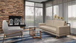 A modern living room with a stone wall, a beige sofa, a grey armchair, and two small tables. - Fairfield Inn & Suites Jeffersonville I-71 (Jeffersonville)