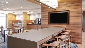 A modern hotel lobby with a long bar, seating area, and a flat-screen TV mounted on a wooden wall. - Fairfield Inn & Suites Jeffersonville I-71 (Jeffersonville)