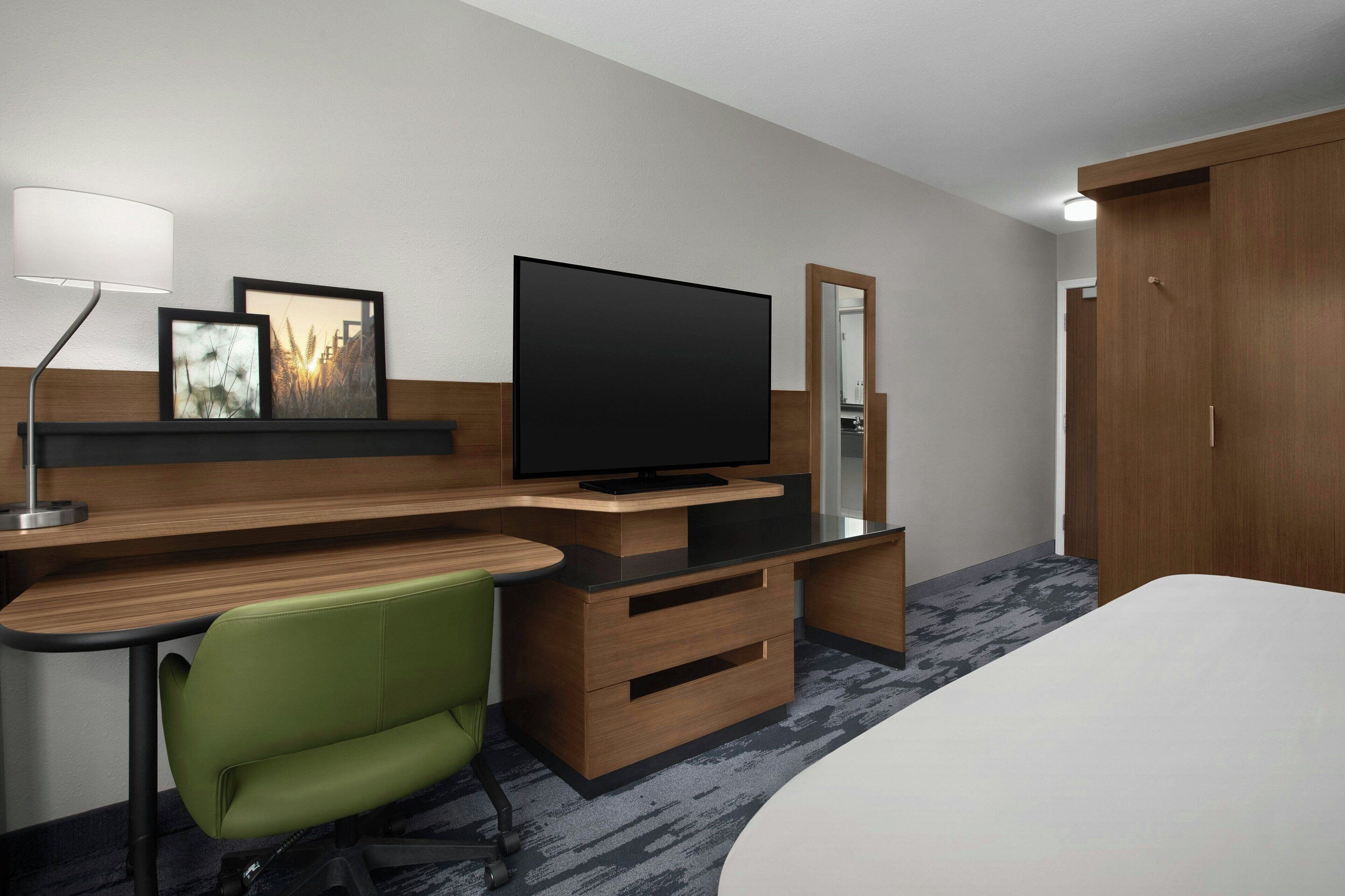 Une chambre d’hôtel comprenant un lit, un bureau avec une chaise, une télévision, un miroir et une armoire.