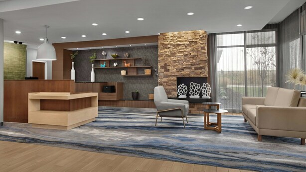 A modern lobby with a reception desk, seating area, stone accent wall, and large windows. - Fairfield Inn & Suites Jeffersonville I-71 (Jeffersonville)