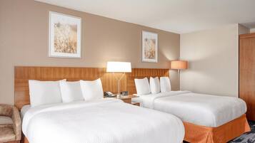 A hotel room with two beds, a wooden headboard, a nightstand, a lamp, and two framed pictures on the wall.