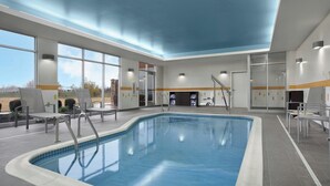 An indoor swimming pool with clear blue water, surrounded by a tiled floor and walls, with large windows allowing natural light and views of the outdoors. - Fairfield Inn & Suites Jeffersonville I-71 (Jeffersonville)