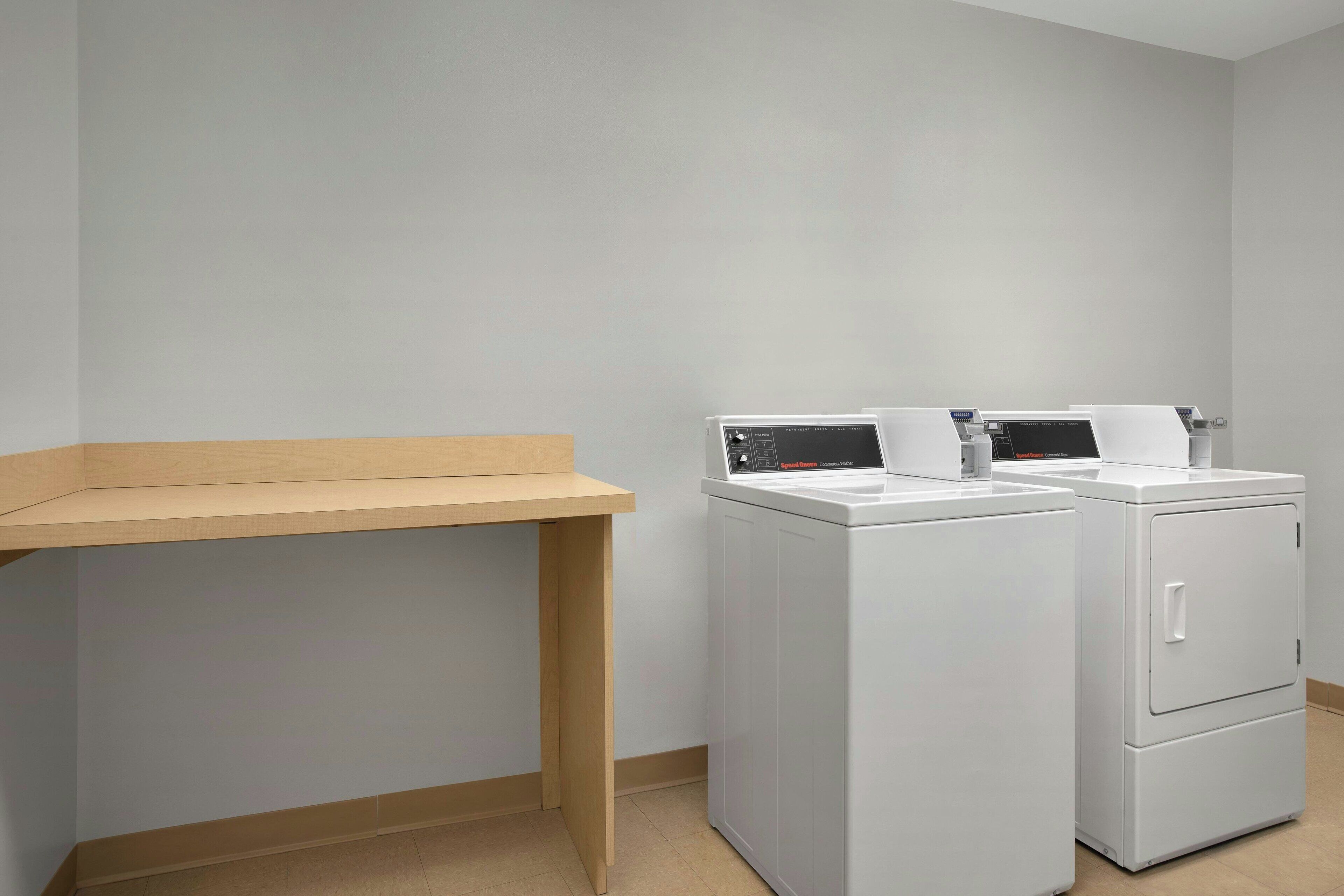 A laundry room with two white washing machines and a wooden bench.